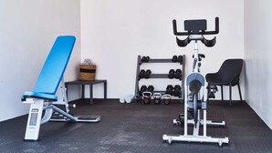 Un gimnasio con equipo de ejercicio, incluyendo una banca, mancuernas y una máquina de pesas.
