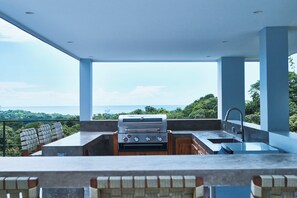 Eine Außenküche mit Grill, Spüle und Sitzgelegenheit mit Blick auf eine schöne Landschaft.