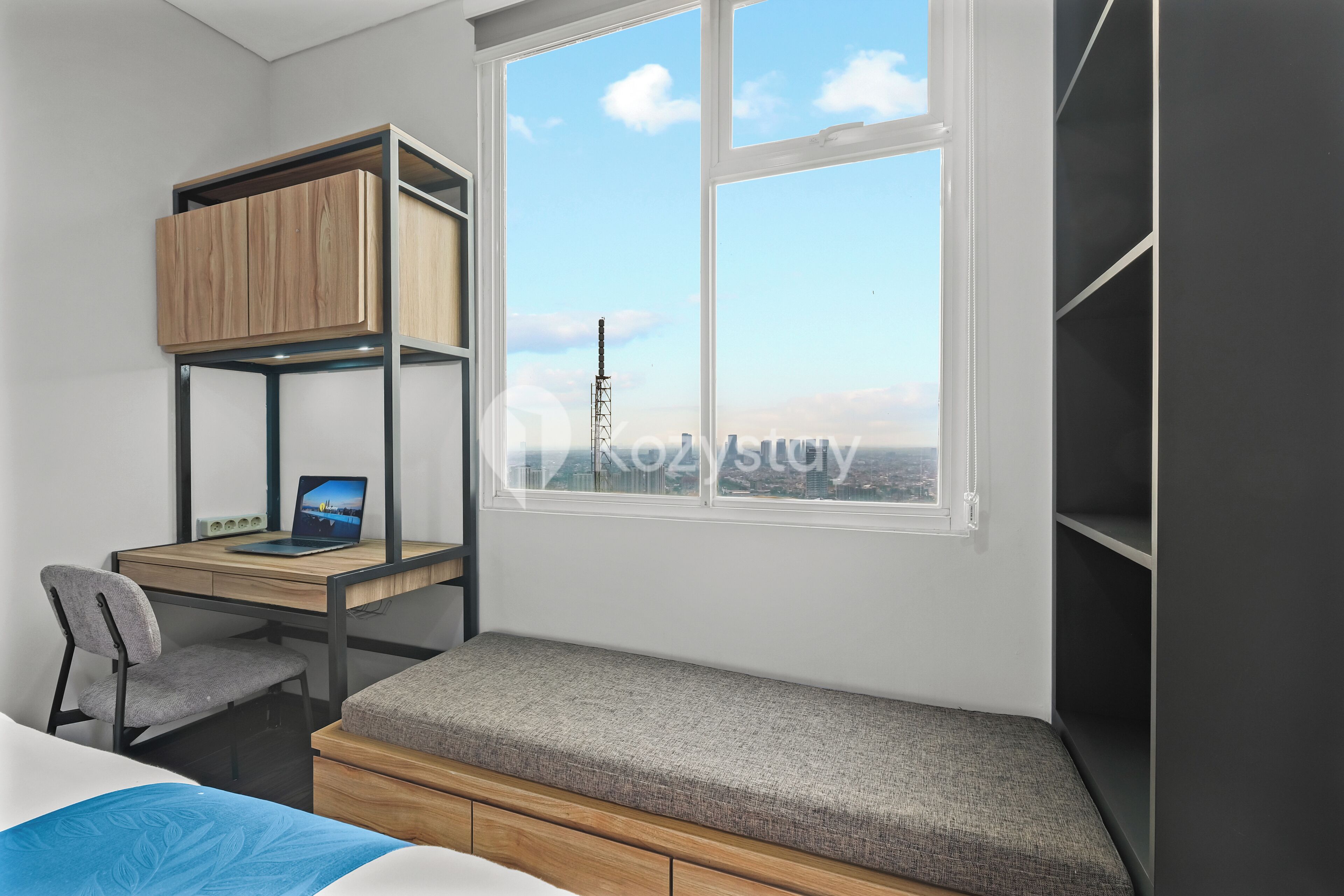 A bedroom with a bunk bed, a desk with a laptop, a chair, and a window with a city view.
