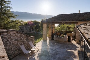 A stone patio with a pergola, outdoor seating, and a view of mountains and a lake.
