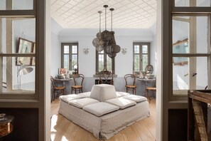 A room with a large cushioned seating area, a chandelier, and multiple windows.