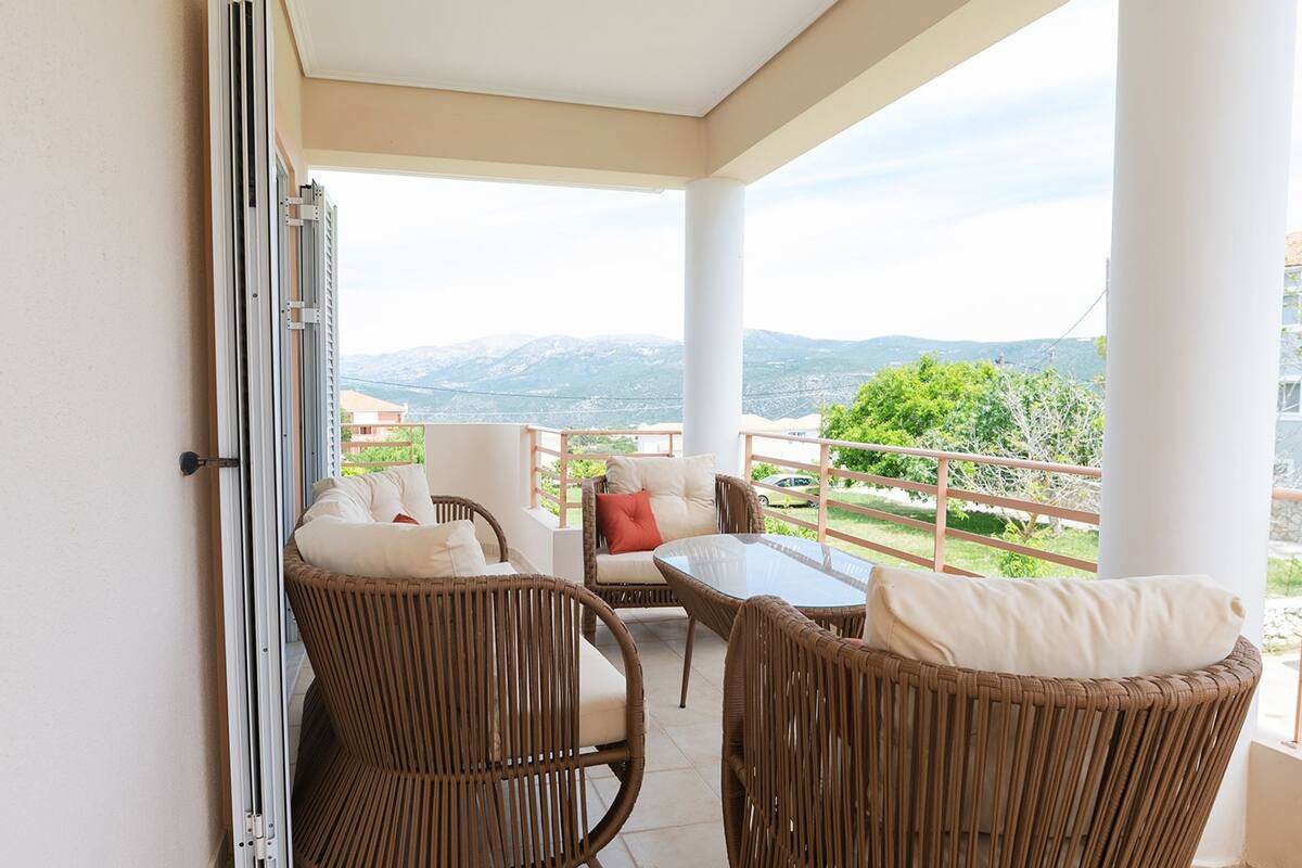 Un balcon doté de meubles en osier, d’une table en verre et offrant une vue sur les montagnes.