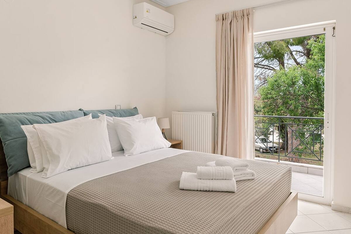 Une chambre à coucher moderne avec un lit en bois, une literie blanche et une vue sur l’extérieur grâce à une grande fenêtre.