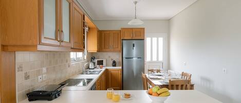 A modern kitchen with wooden cabinets, a stainless steel refrigerator, a dining area with a table and chairs, and a white countertop with breakfast items.