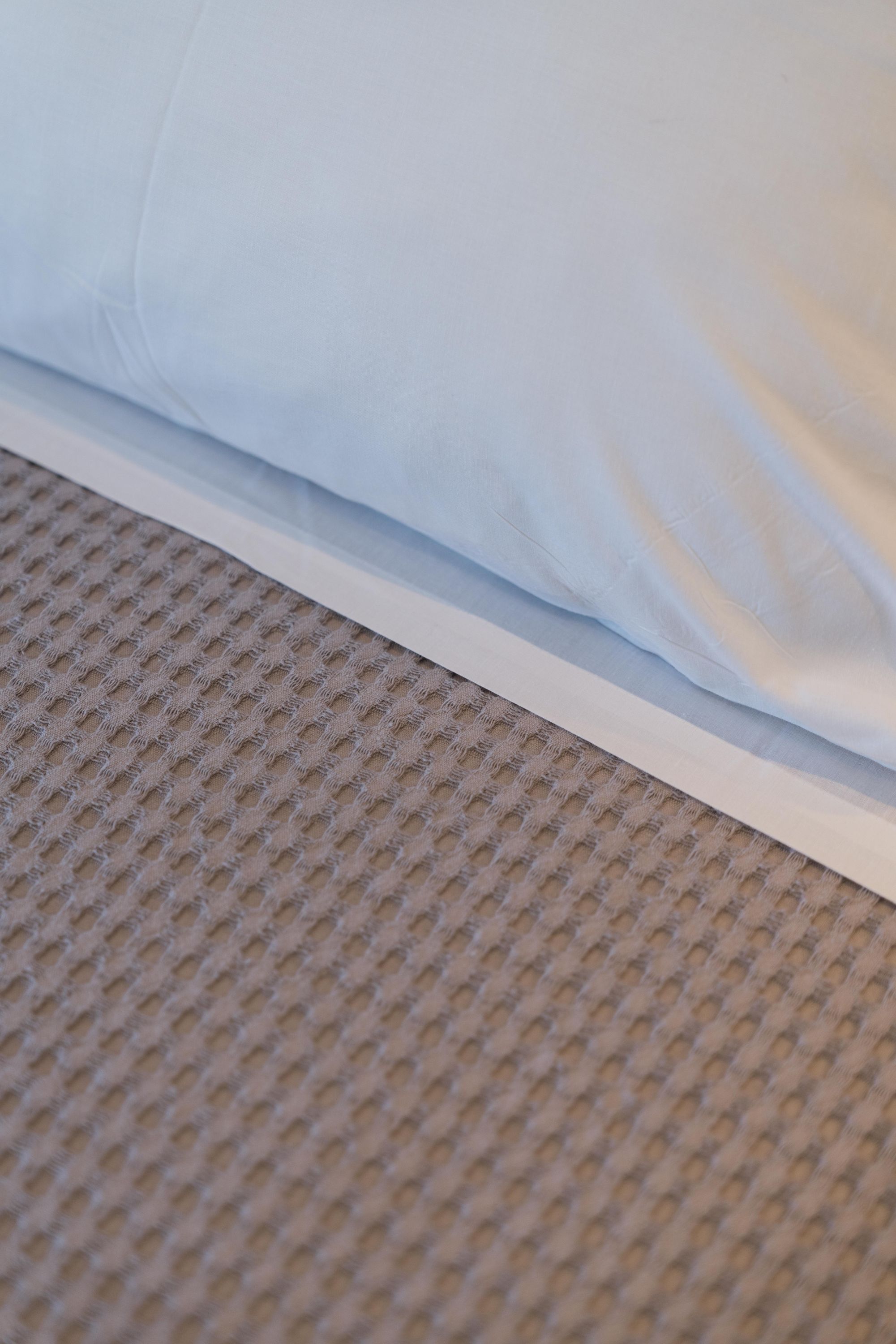 Een detail van een bed met een wit laken en een geruwd beigekleurig tapijt.