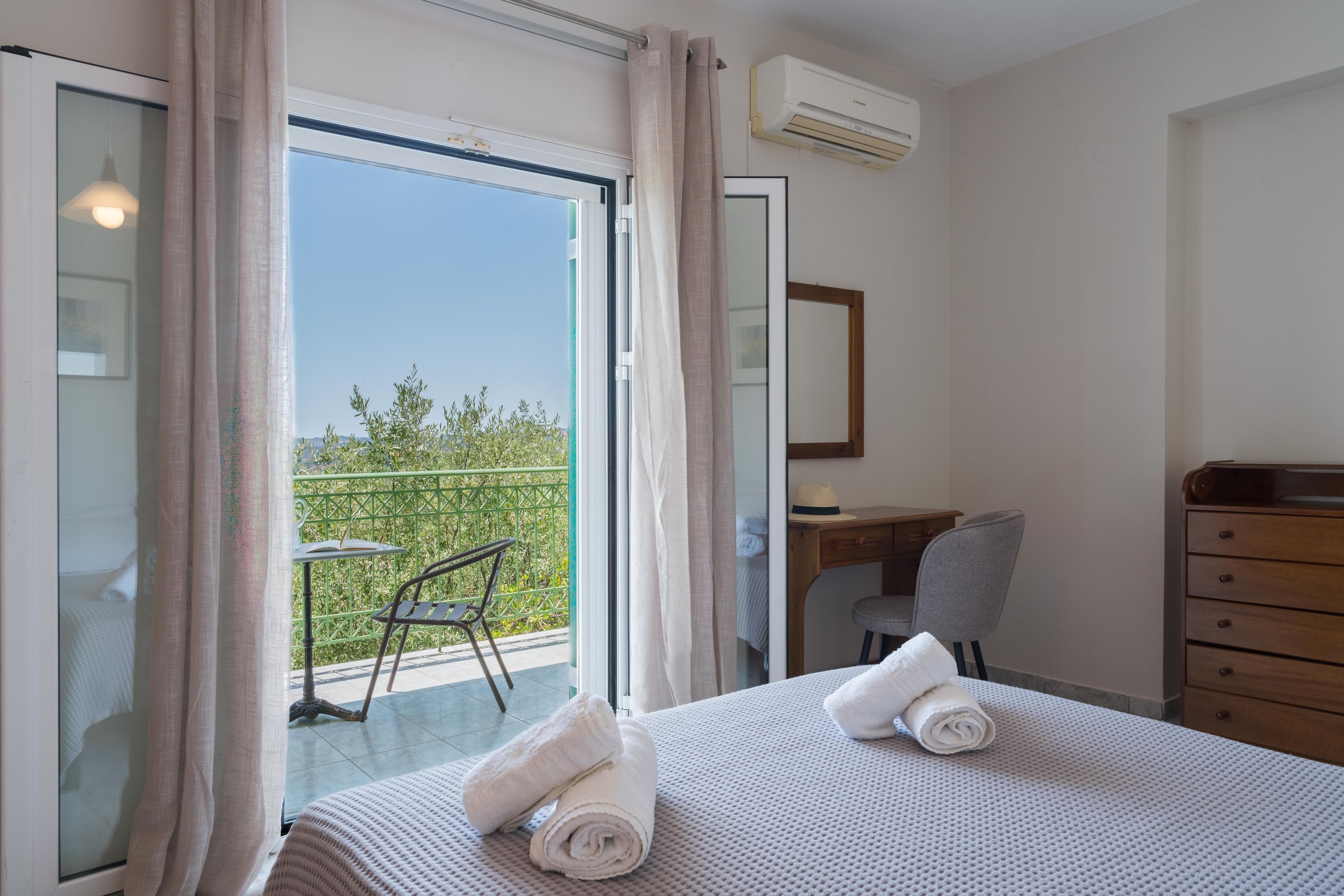 A hotel room with a bed, a desk, a chair, and a balcony with a table and chairs.