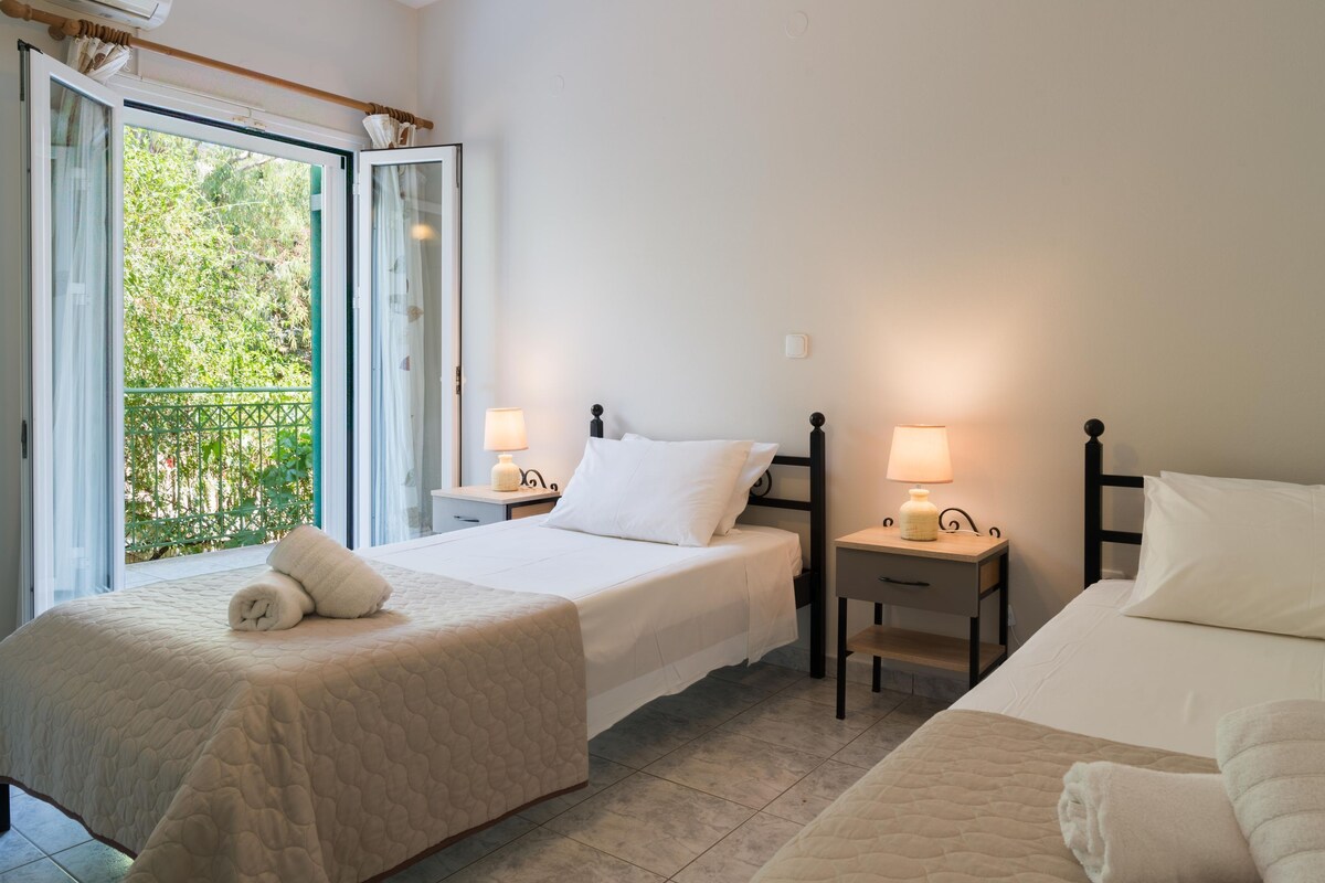 A hotel room with two beds, a balcony, and two bedside tables with lamps.