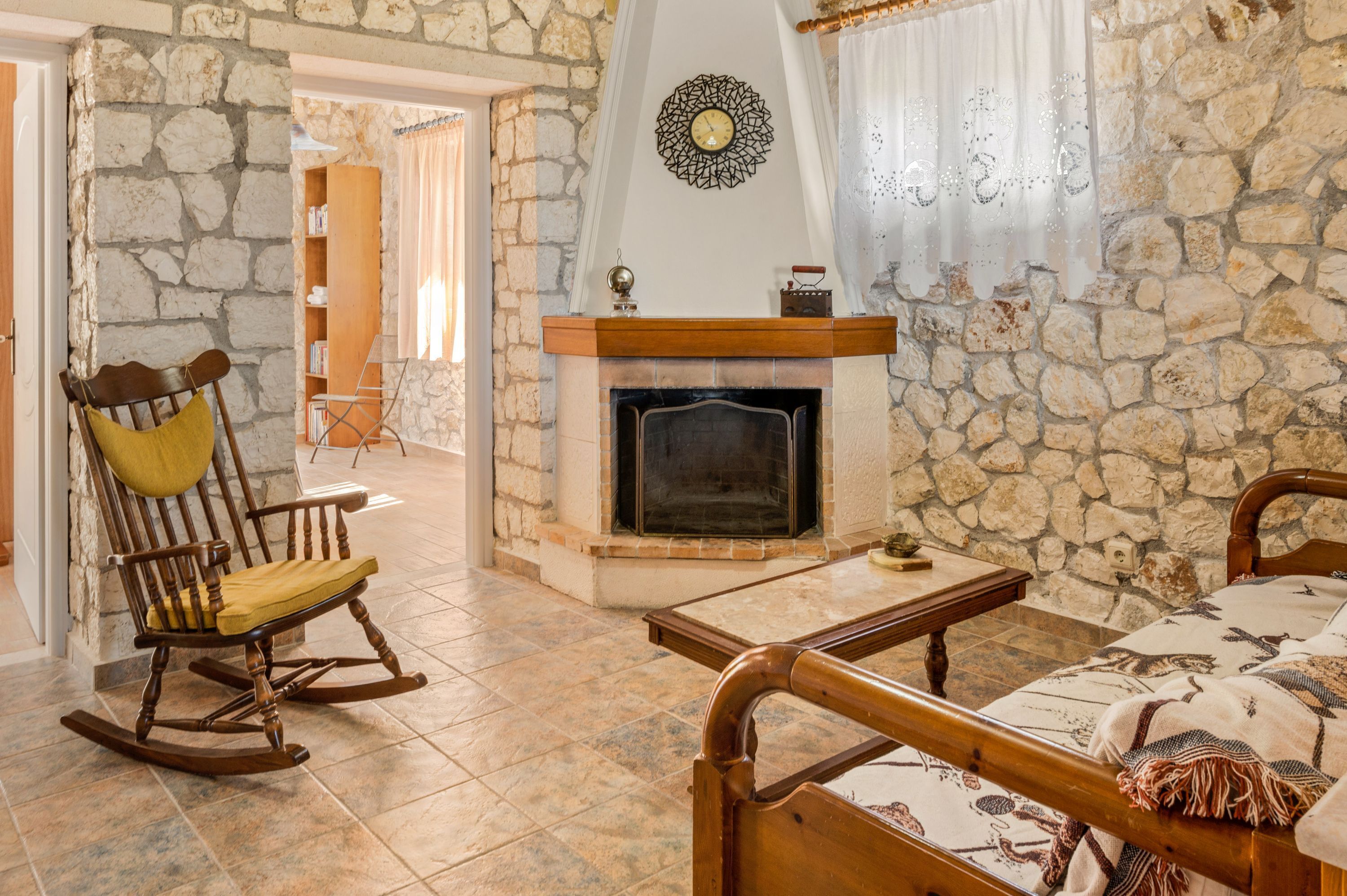 A cozy room with a stone wall, a fireplace, a rocking chair, and a bed with a patterned blanket.