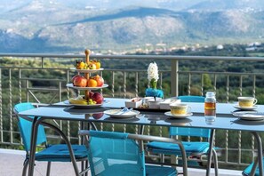 A table set outdoors with a mountain view, featuring a fruit platter, plates, cups, and a vase with a white flower. - Belle Helen s Villa - 3 Bedrooms Billiard Pool (Kefalonia)