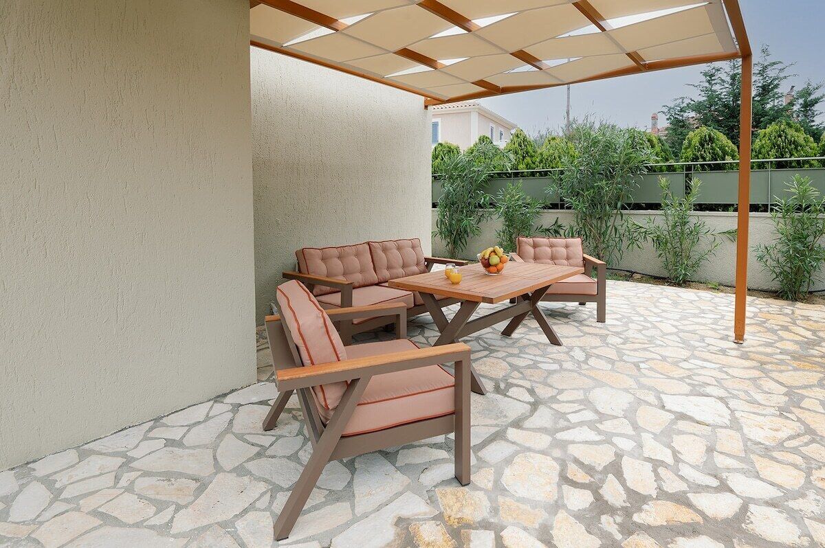 An outdoor patio with stone flooring, a wooden table, and cushioned chairs.