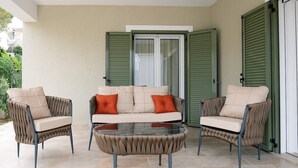 Un patio con un sofá color beige, dos sillones y una mesa de centro de vidrio.