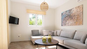 Una sala de estar moderna con un sofá color beige, una mesa de centro redonda y un televisor de pantalla plana montado en la pared.