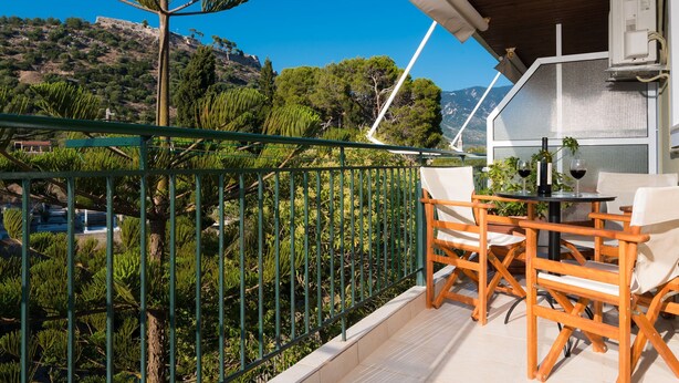 A balcony with a view of a mountainous landscape, wooden furniture, and a table with glasses.