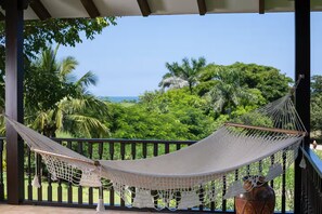 Una hamaca en un balcón con vista a palmeras y al océano.