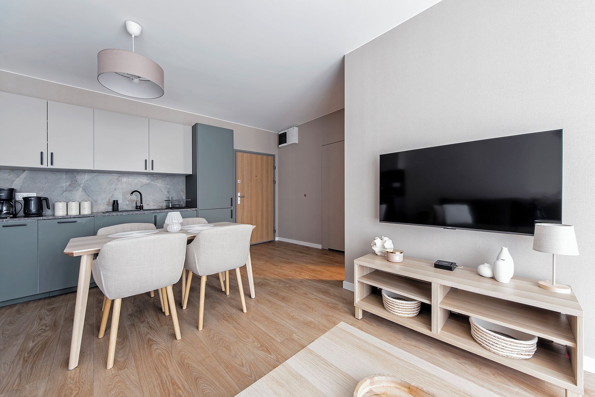 Uma cozinha moderna com armários cinzas, bancada de mármore e um espaço de refeições com mesa e cadeiras.
