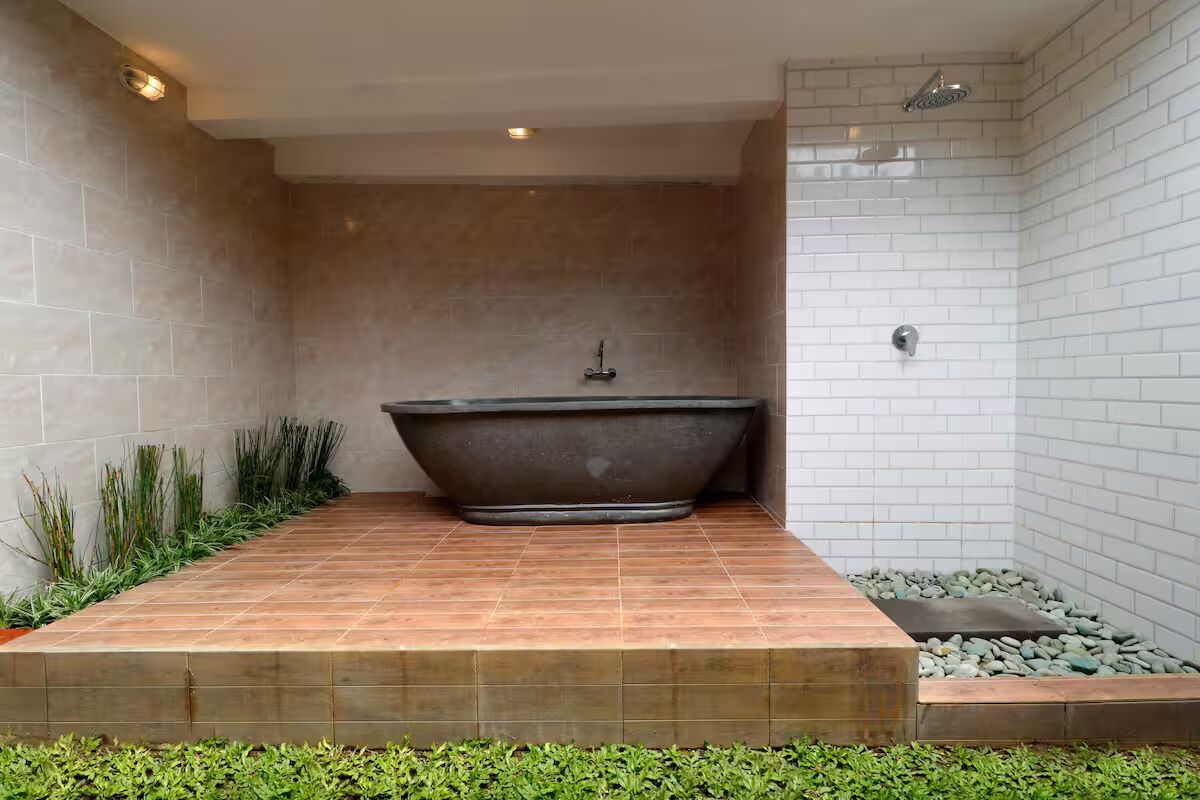A modern bathroom with a freestanding bathtub, a shower area, and a small garden space with plants.
