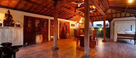 A spacious room with wooden flooring, a bed with white curtains, a dining area with a table and chairs, and a statue on a shelf.