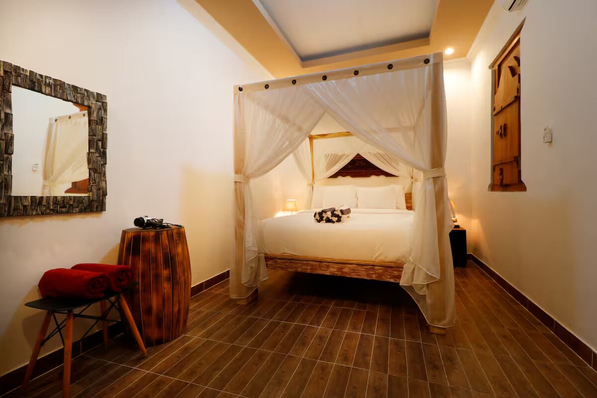 Un dormitorio con una cama de dos columnas con dosel, una mesita de madera y una silla roja.