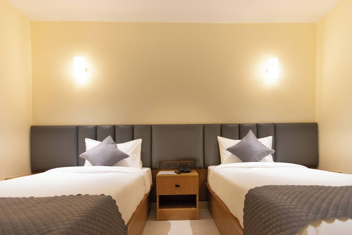 A hotel room with two beds, a nightstand, and two wall-mounted lights.
