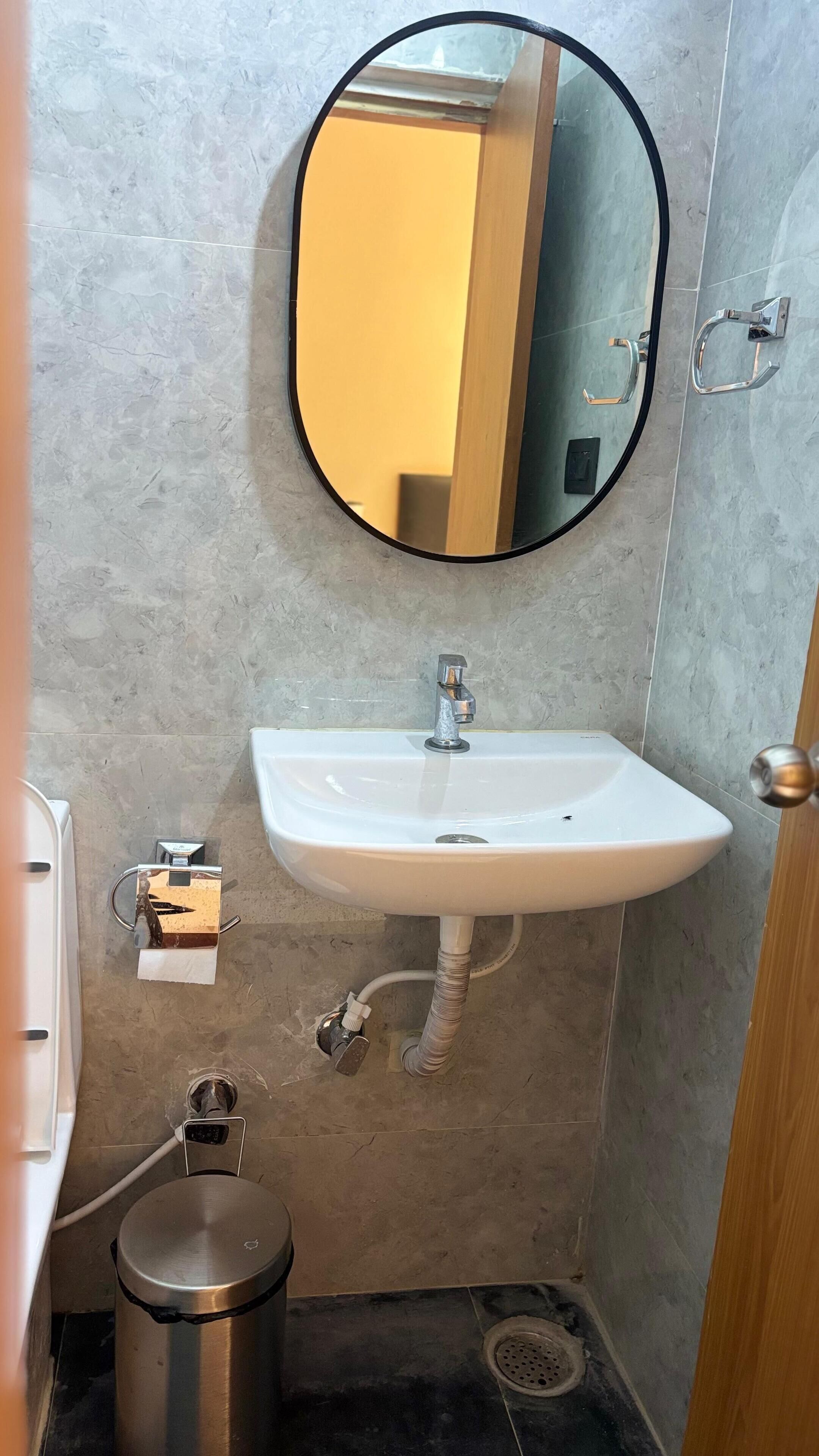 A bathroom with a white sink, a round mirror, and a stainless steel trash can.