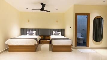 A hotel room with two beds, a ceiling fan, a wooden headboard, and a view of the bathroom.