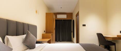 A hotel room with a large bed, a desk, a chair, and a wardrobe.