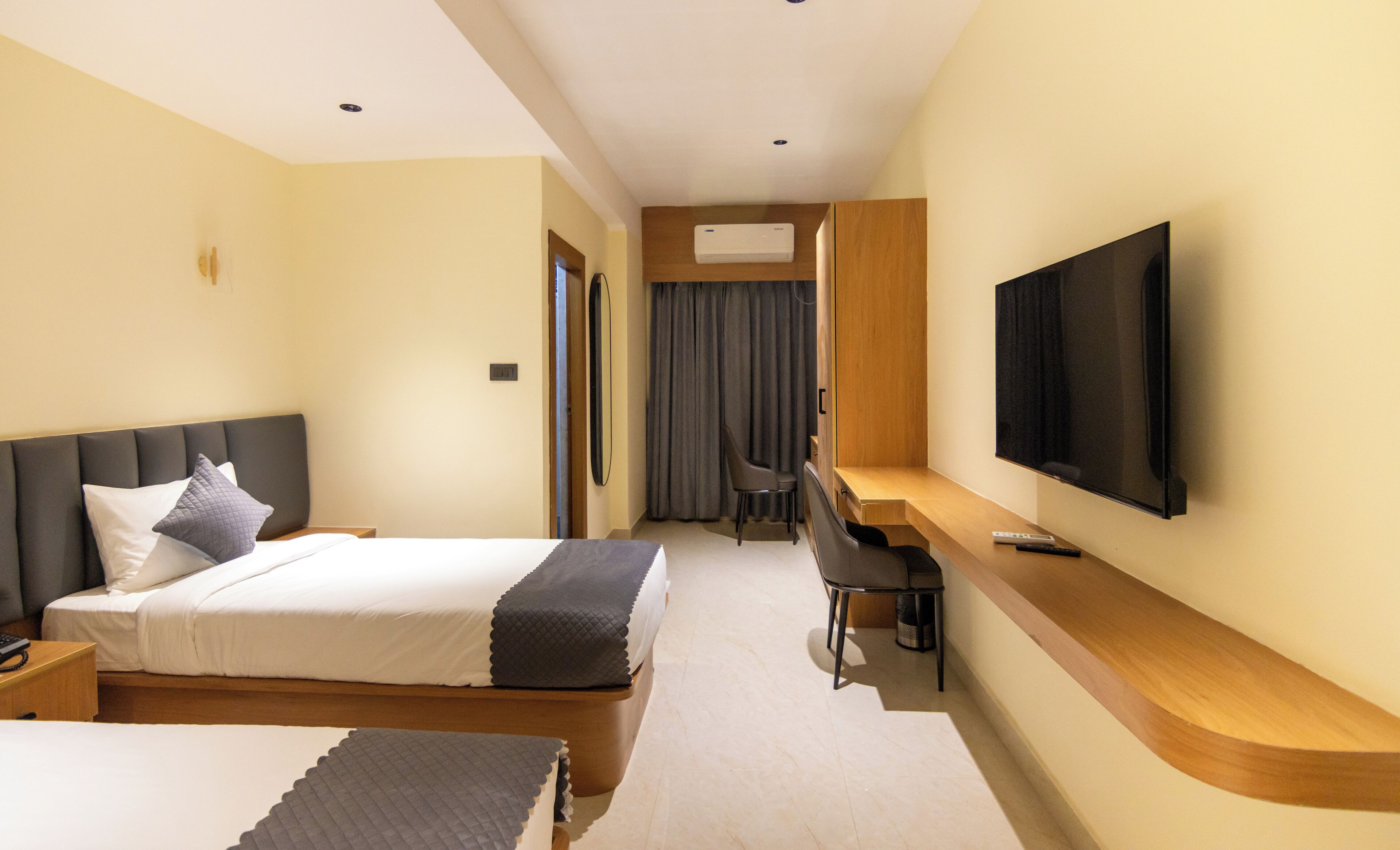 Una camera d'albergo con un letto, una scrivania, una sedia, una TV e una finestra con tende.