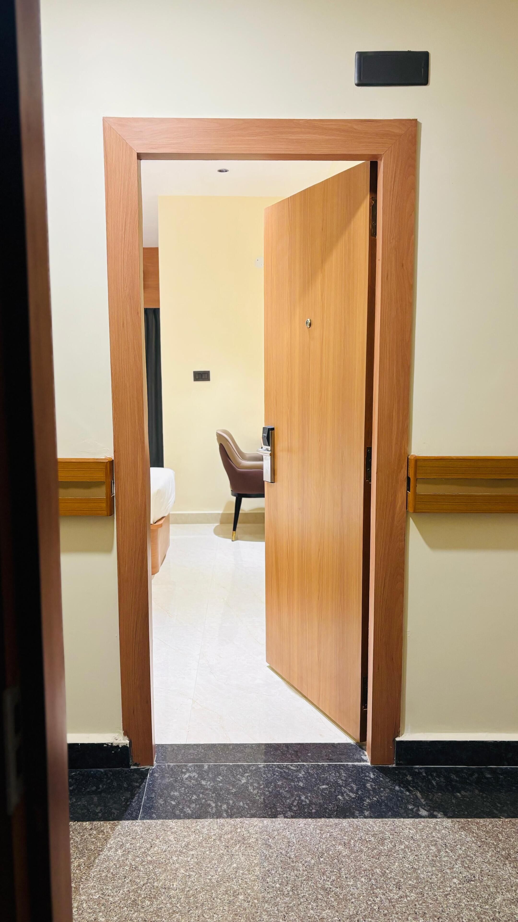 Habitación de hotel con puerta de madera, cama, sillón y una mesita.