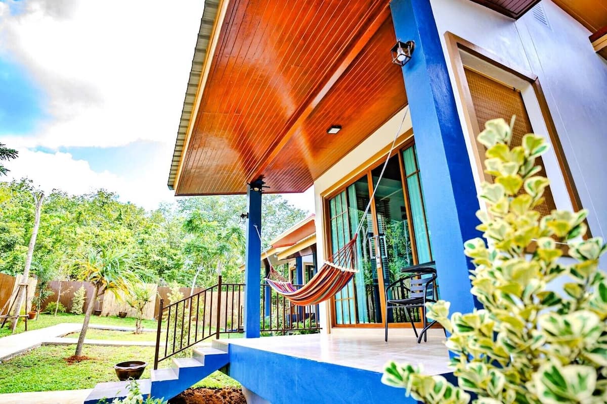 A modern house with a blue exterior, a wooden deck, and a hammock.