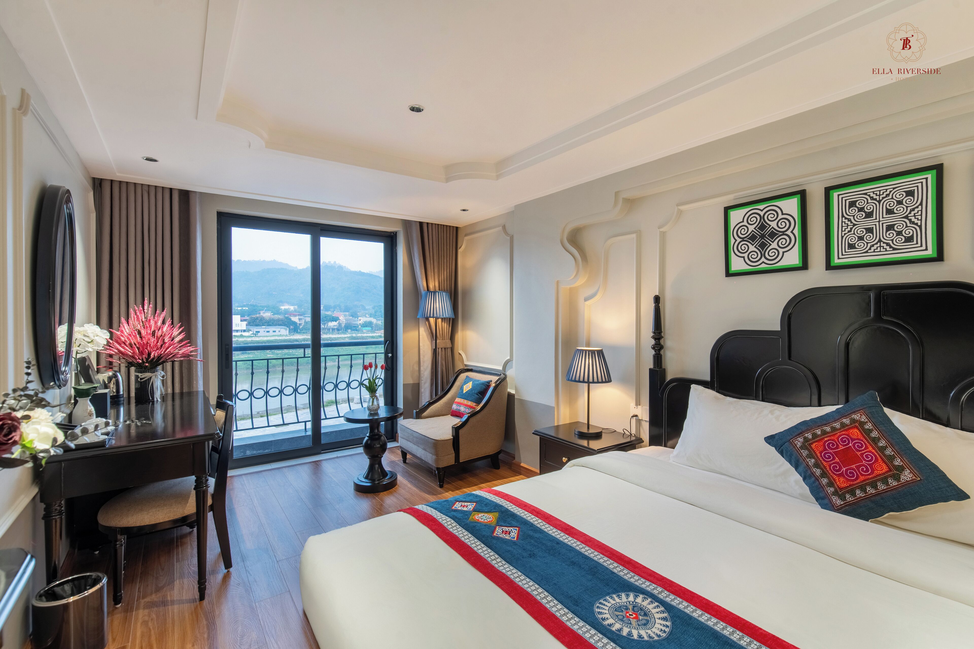A hotel room with a bed, a desk, a chair, a lamp, and a view of the city.