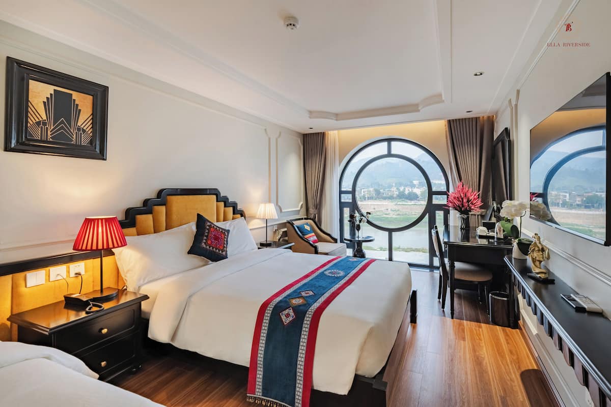 Habitación de hotel con una cama grande, un escritorio, una silla, una mesita de noche, una lámpara, una ventana con vistas y un cuadro en la pared.