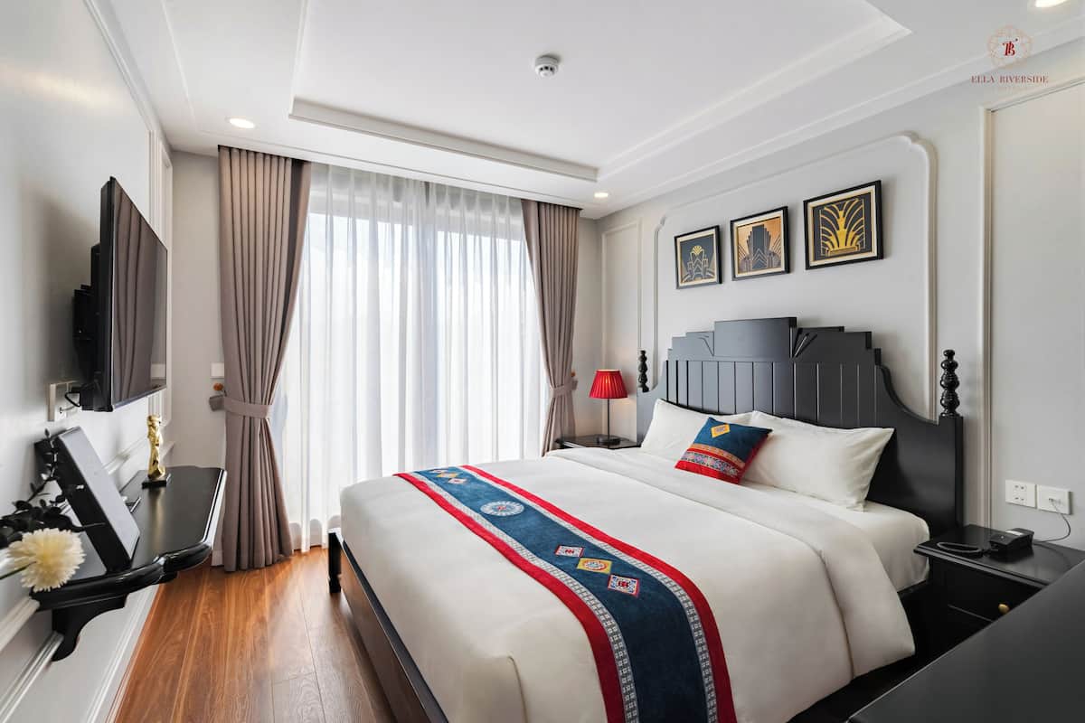 Una habitación de hotel con una cama grande, un televisor de pantalla plana, un escritorio con lámpara y una ventana con cortinas.