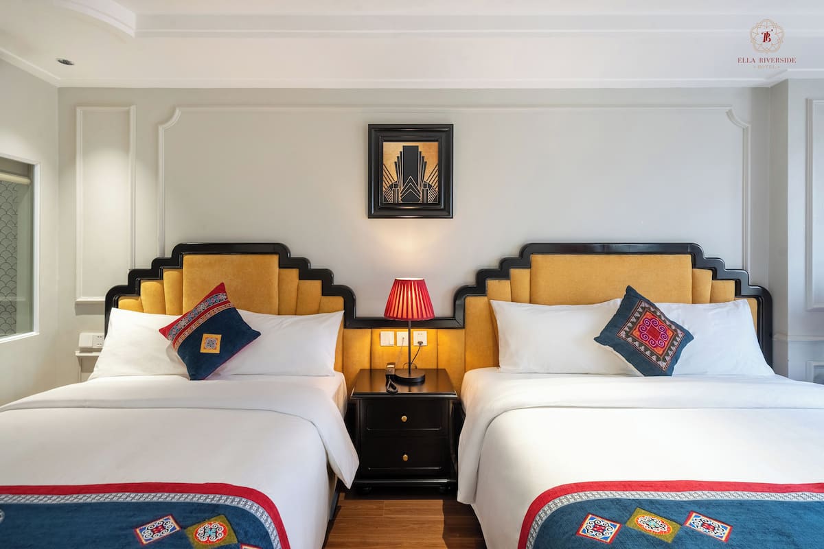 Habitación de hotel con dos camas, una mesita de noche con lámpara y un cuadro enmarcado en la pared.