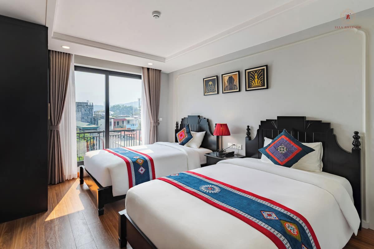 Habitación de hotel con dos camas, un ventanal grande y vistas a la ciudad.
