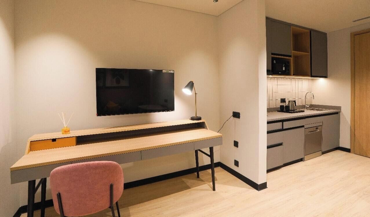 Une chambre moderne équipée d’un bureau, d’une chaise, d’une télévision et d’une kitchenette.
