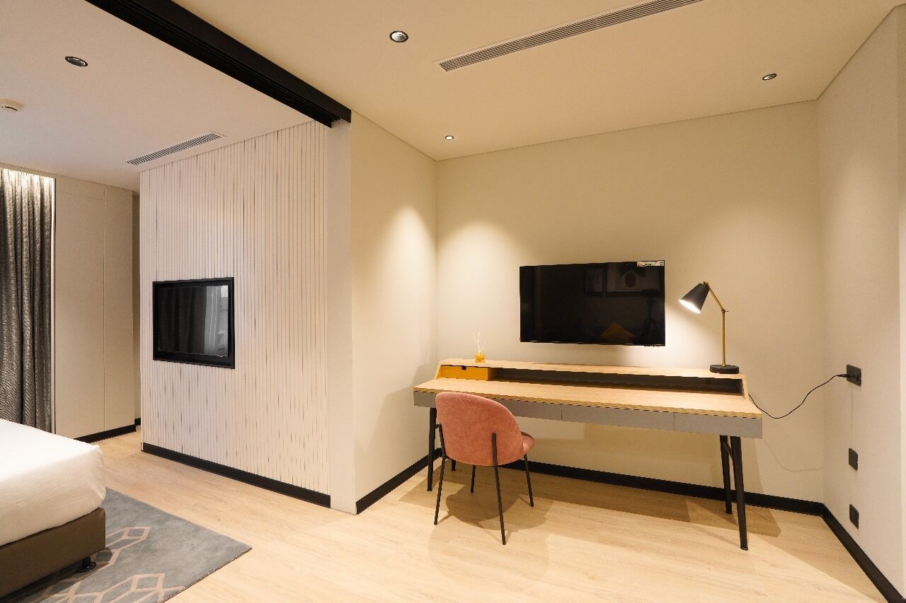Una habitación de hotel moderna con una cama, un escritorio con silla, un televisor de pantalla plana en la pared y una lámpara.