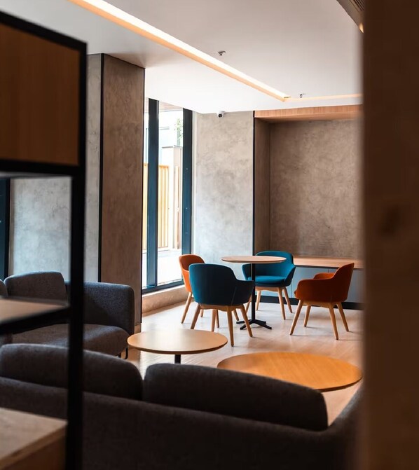 Een modern interieur met een zithoek met banken en tafels, grote ramen met natuurlijk licht, en een minimalistisch ontwerp.