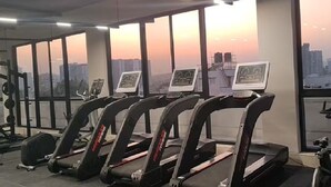 A gym with treadmills, weight machines, and a view of the city at sunset. - Orchid Parc by evaddo stays (Bengaluru)