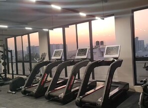 Een fitnessruimte met loopbanden, krachttoestellen en uitzicht op de stad bij zonsondergang.