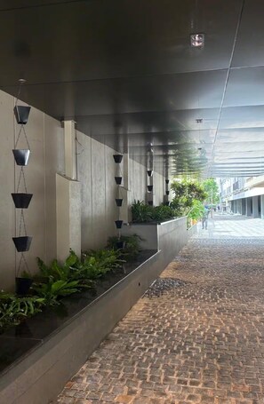 A covered walkway with hanging planters and a cobblestone path. - Orchid Parc by evaddo (Bengaluru)