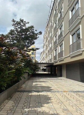 A paved walkway between buildings with a tree-lined path and a clear sky. - Orchid Parc by evaddo stays (Bengaluru)