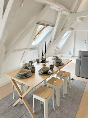 A dining area with a wooden table set for four, white walls, and a sloped ceiling with skylights. - 2BR Apartment with Canal View in Ghent (Ghent)
