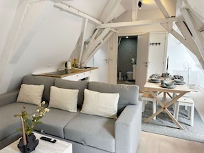 Een moderne loftkamer met een grijze bank, een eettafel en een keukenhoek.