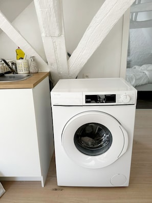 A compact, white washing machine in a modern kitchen with a wooden countertop and a small sink. - 2BR Apartment with Canal View in Ghent (Ghent)