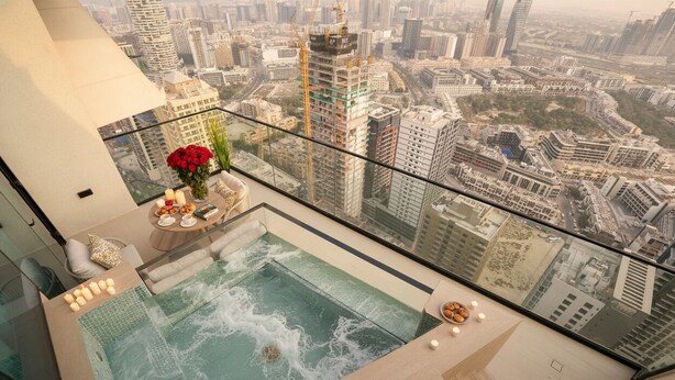 Ein Infinity-Pool auf dem Dach mit Blick auf die Stadt, einer Glasbrüstung und einem Tisch mit Kerzen und Snacks.