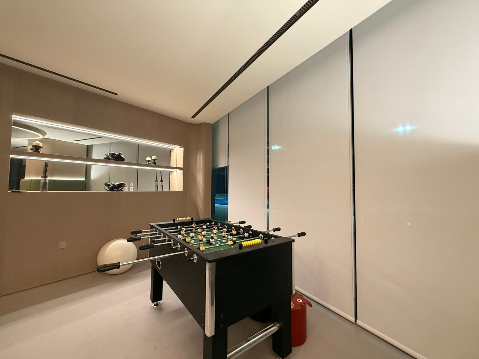 A modern room with a foosball table, a mirror, and a red trash bin.