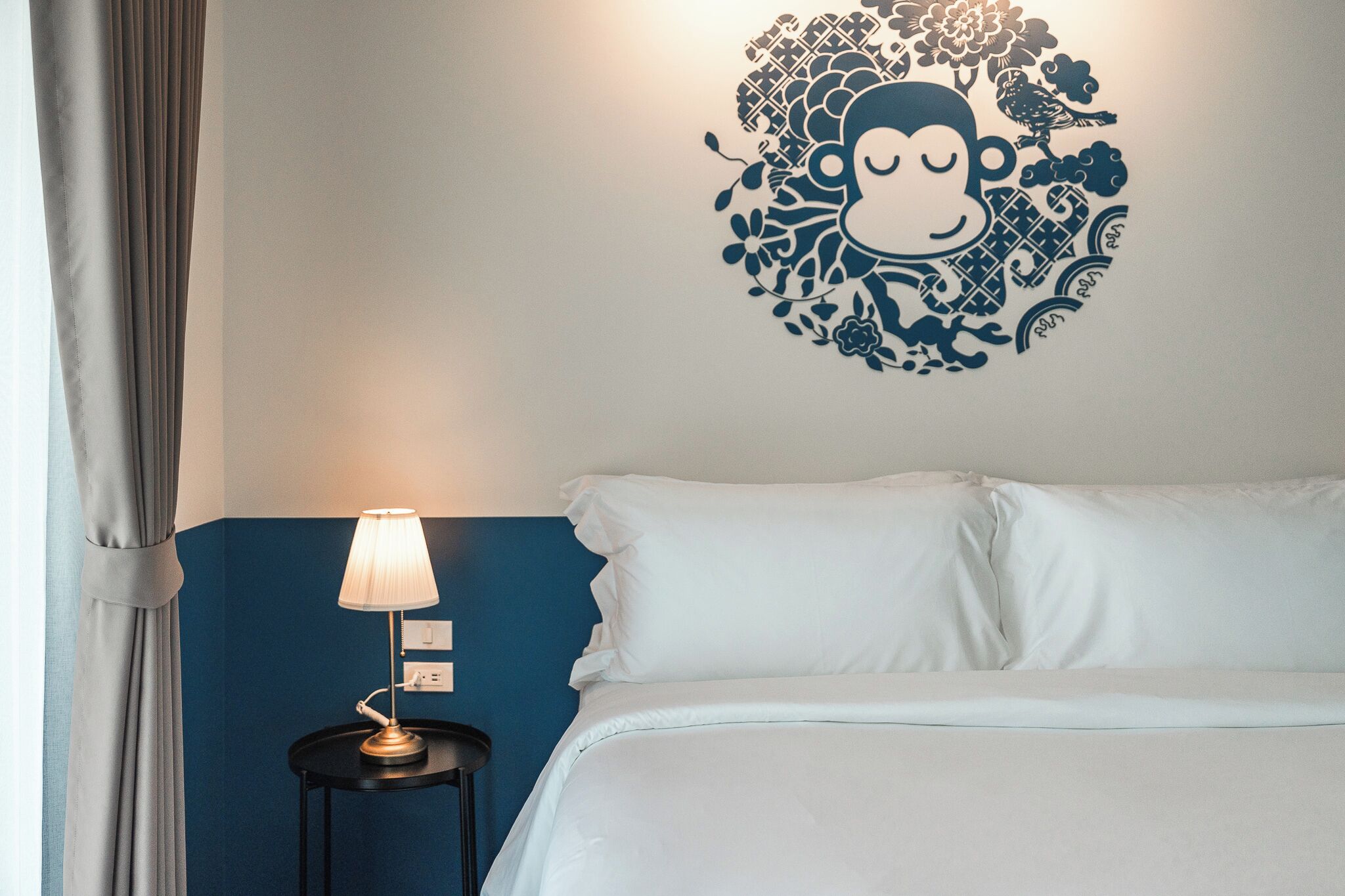 A hotel room with a bed, a nightstand with a lamp, and a wall decoration.
