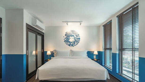 Een hotelkamer met een groot bed, nachtlampjes, een wandairconditioner en een raam met jaloezieën.