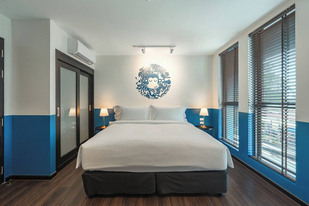 Ein Hotelzimmer mit einem großen Bett, Nachttischlampen, einer Wand-Klimaanlage und einem Fenster mit Jalousien.