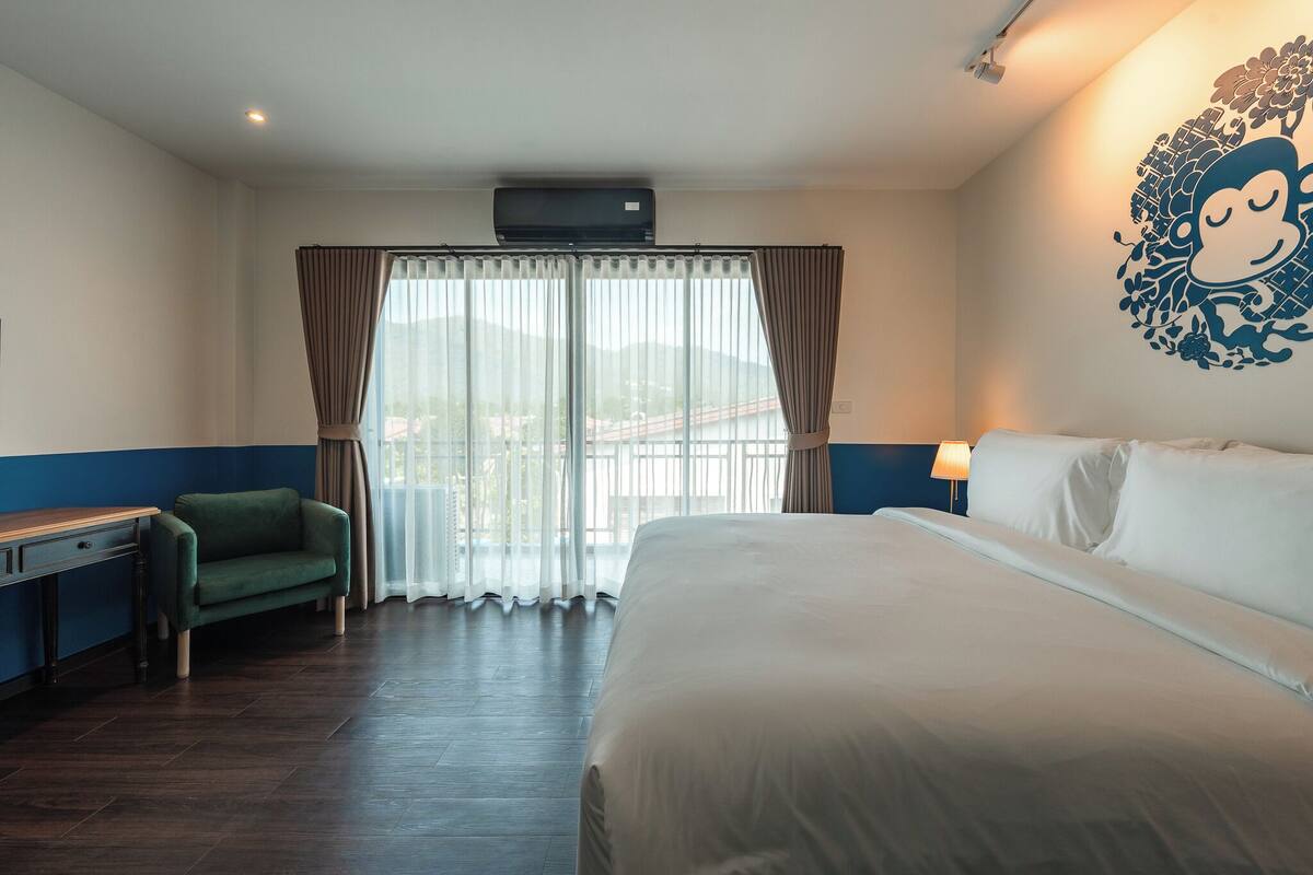 Ein Hotelzimmer mit Bett, Schreibtisch, Stuhl und einem großen Fenster mit Vorhängen.